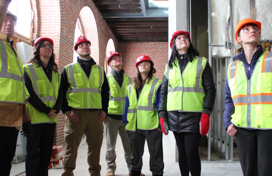 Students in hard hats and reflecting vests observing architecture